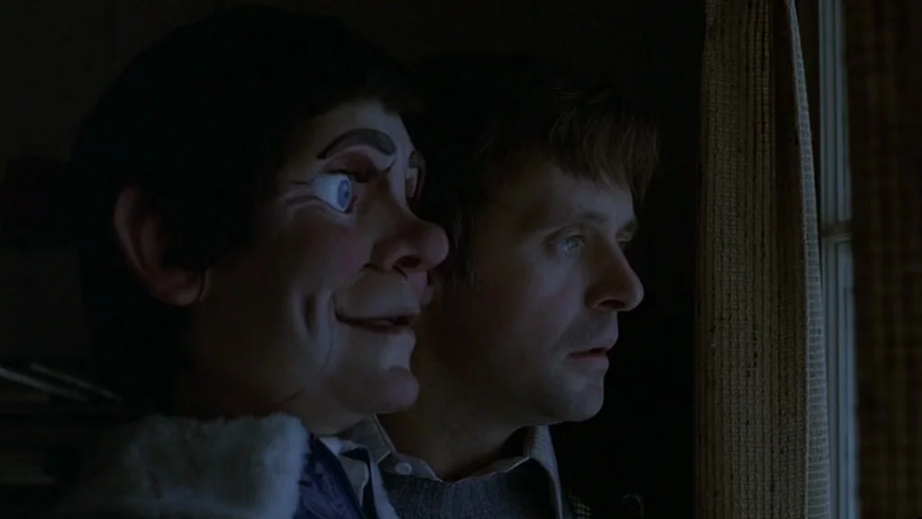 Magic (1978) movie still: closeup — A dimly lit room at night features a man standing beside a window. Next to him, a ventriloquist dummy with a…