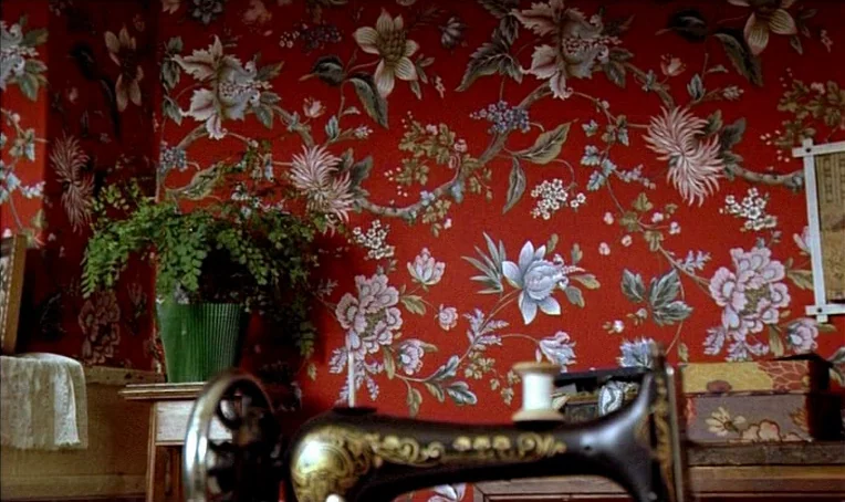 Jacquot de Nantes (1991) movie still: medium — A wall covered in red floral wallpaper provides the backdrop for a sewing room. An antique sewing…