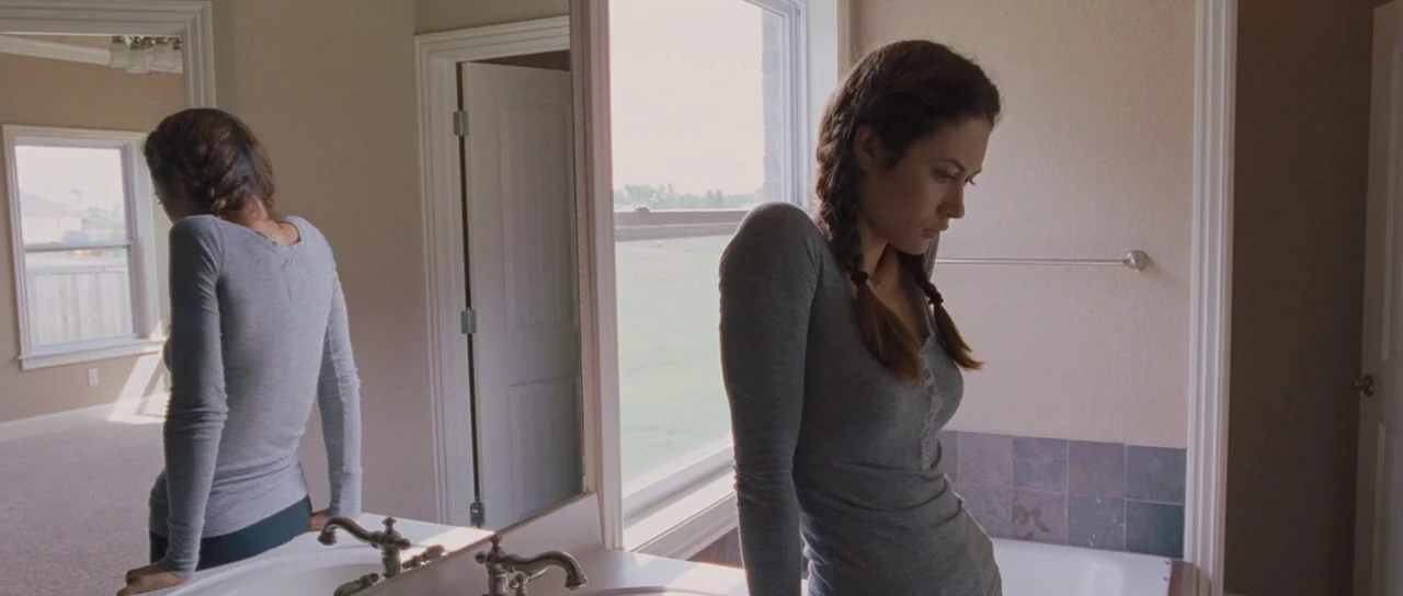 To The Wonder (2012) movie still: medium — A residential bathroom features a large mirror reflecting a window and an adjacent room. A young woman…