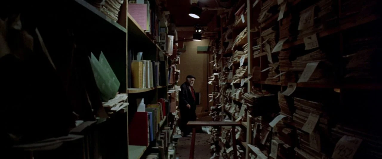 Soylent Green (1973) movie still: wide — A narrow, cluttered archive room features floor-to-ceiling wooden shelves packed with paper documents. An…