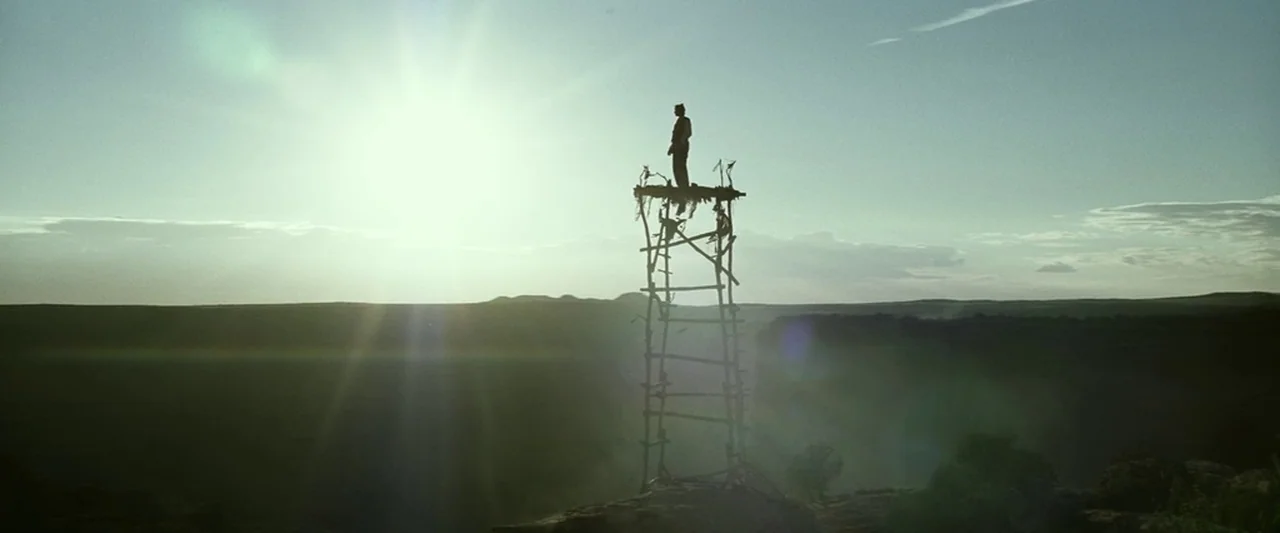 The Lone Ranger (2013) movie still: wide — A tall, primitive wooden lookout tower sits on the edge of a deep canyon. A lone figure stands motionless…