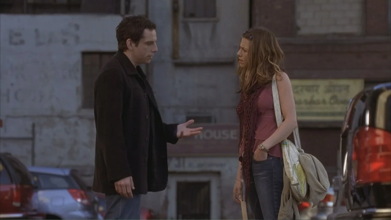 Along Came Polly (2004) movie still: medium — An urban parking lot features weathered brick buildings and parked vehicles in the background. A man…