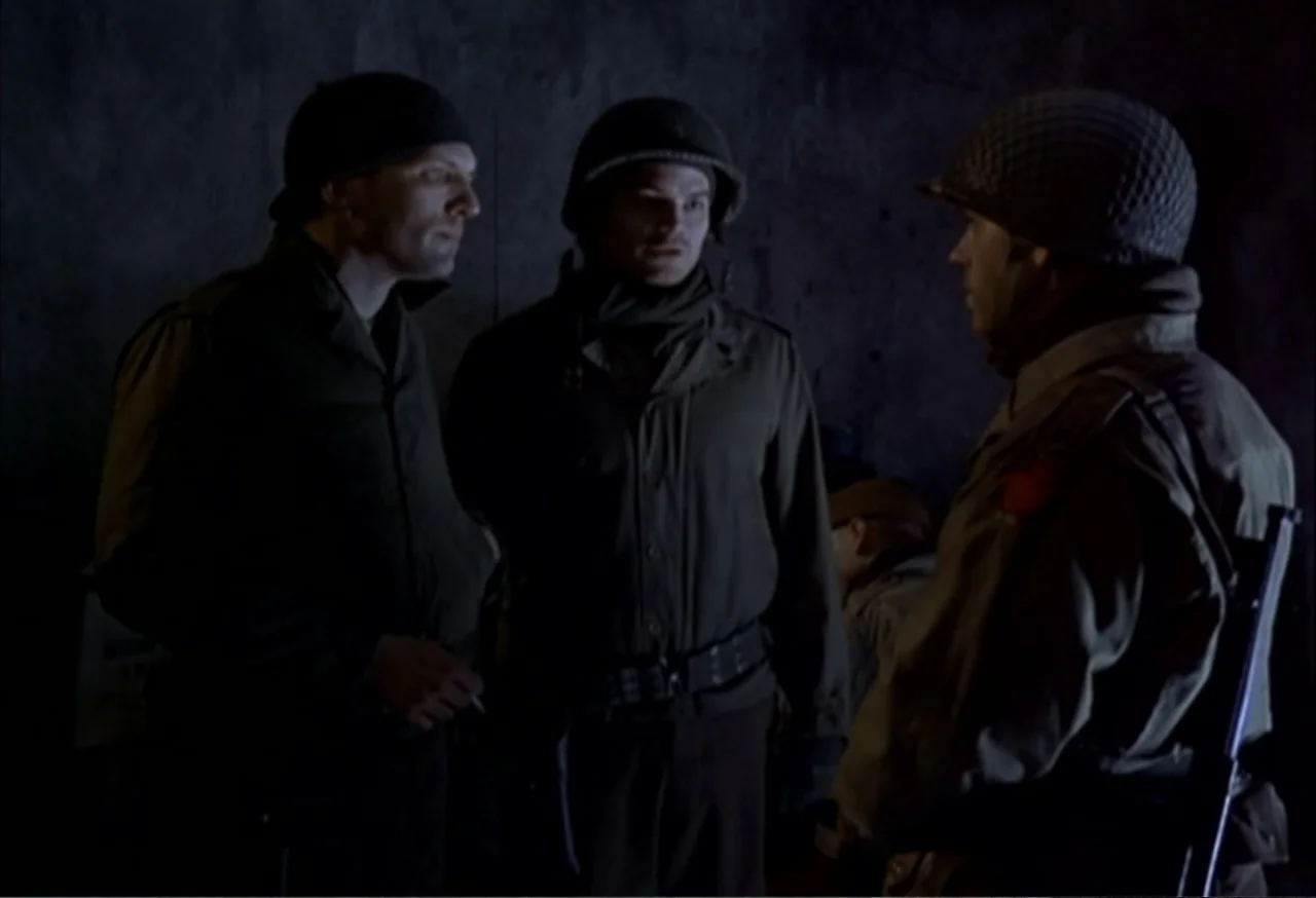 When Trumpets Fade (1998) movie still: medium — A dimly lit concrete bunker interior with rough walls and shadows. Three soldiers in 1940s-era…
