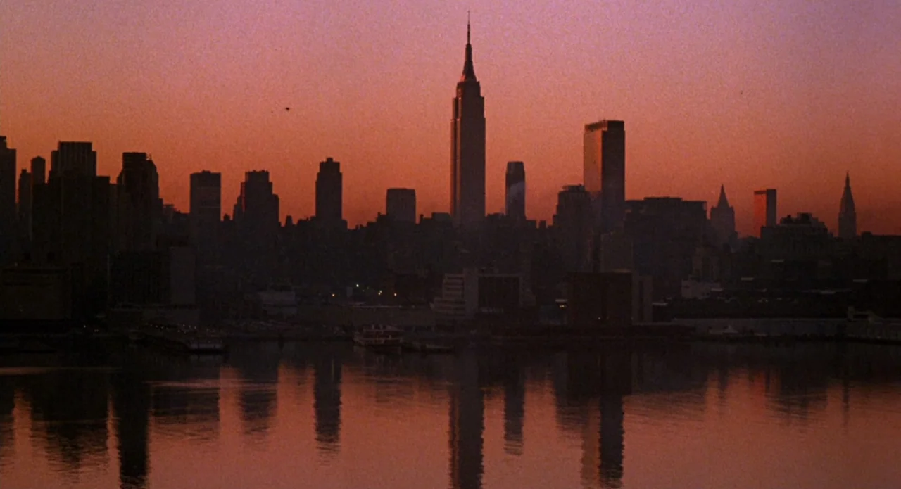 Brain Damage (1988) movie still: establishing — A skyline of a major city is silhouetted against a deep orange sunset sky. The entire scene is…