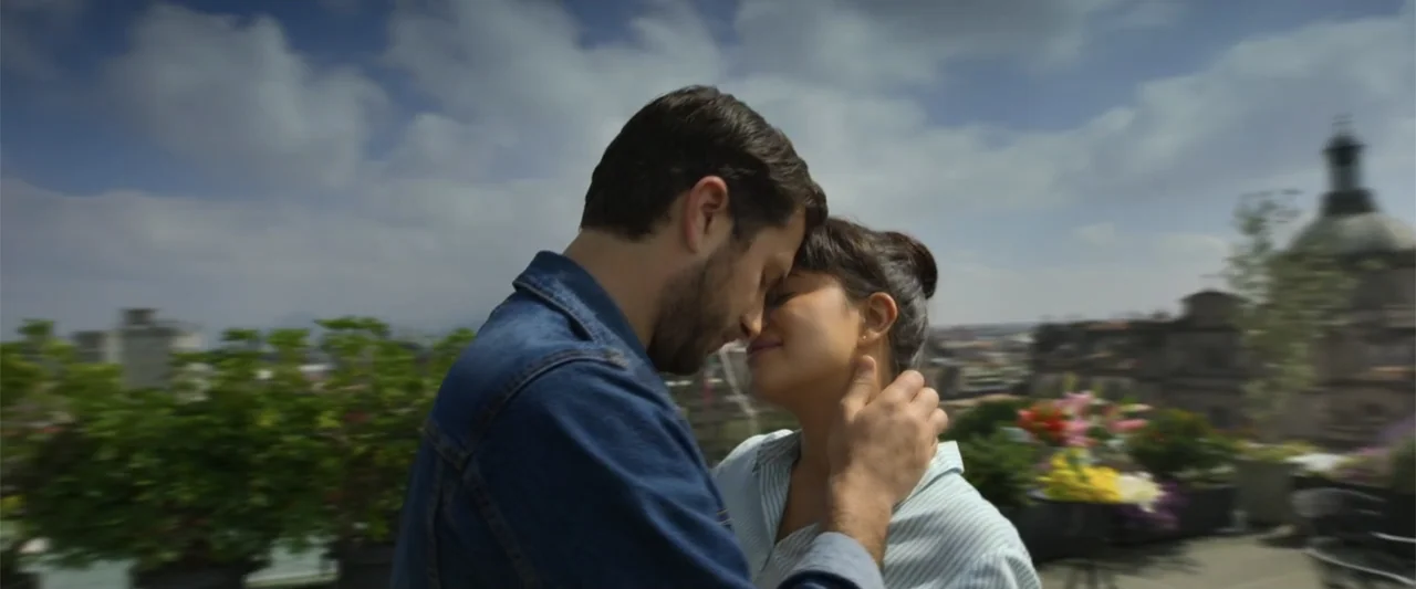 Tequila Re-Pasado (2023) movie still: medium — A rooftop terrace with a city skyline and blurred building architecture in the background. A man and…