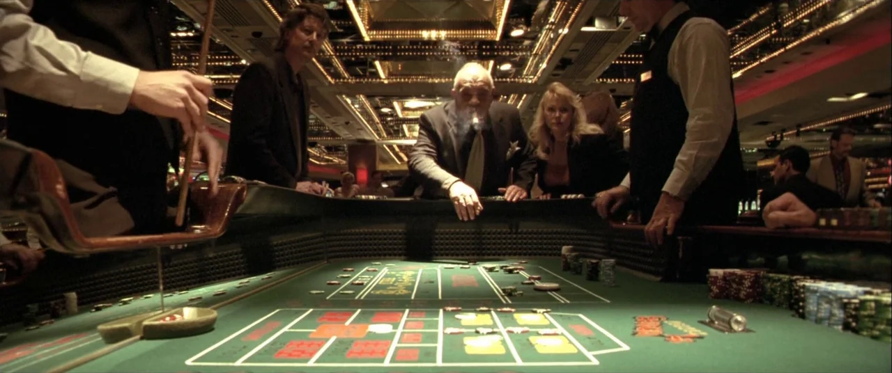 The Cooler (2003) movie still: wide — A green felt table in a brightly lit casino environment. A man in a suit leans over to place a bet.