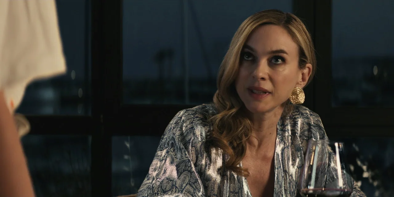 My Fault (2023) movie still: medium — A dimly lit restaurant interior features a large window overlooking a dark exterior area. A woman in a…