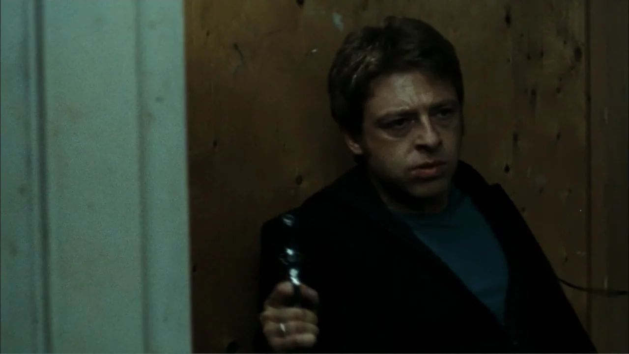 Driven to Kill (2009) movie still: medium — An interior space features a man leaning against a plain plywood wall partition. The subject grips a…