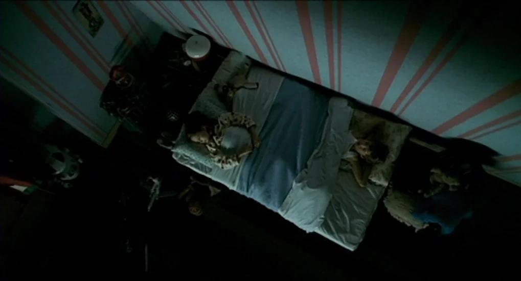 Jeux d’Enfants (2003) movie still: wide — A room features light walls with pink vertical stripes and dark wooden flooring. Two children are lying in…