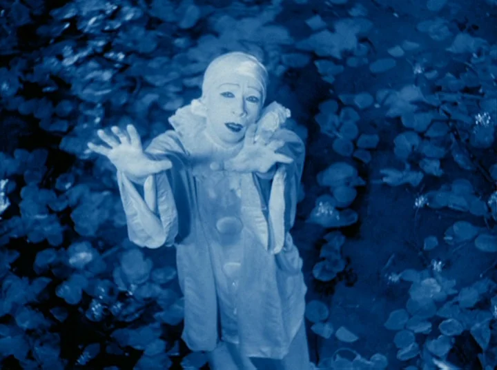Rabbit’s Moon (1950) movie still: medium — A figure dressed as a pierrot stands in a pond covered with floating leaves. The clown extends both hands…