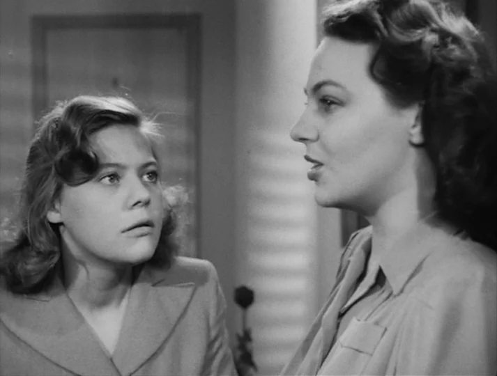Port of Call (1948) movie still: medium — An interior space with a door frame and a single rose visible in background. Two women stand facing each…