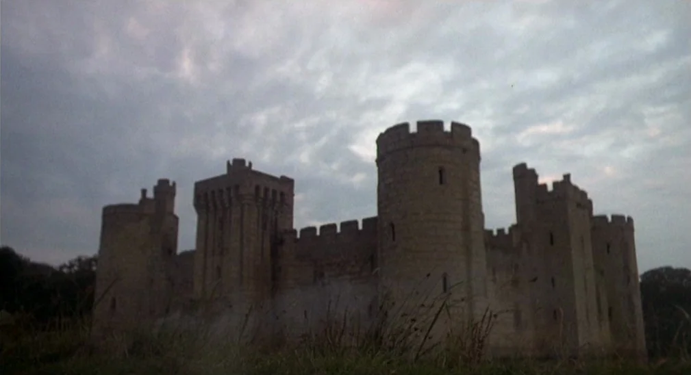 Monty Python and the Holy Grail (1975) movie still: establishing — A stone castle with multiple towers and crenellations sits against a heavy…