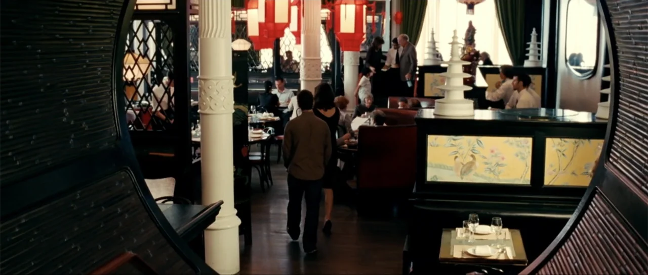 The Rebound (2009) movie still: medium — An upscale dining space features dark wood accents, decorative yellow panels, and hanging red lanterns. A…