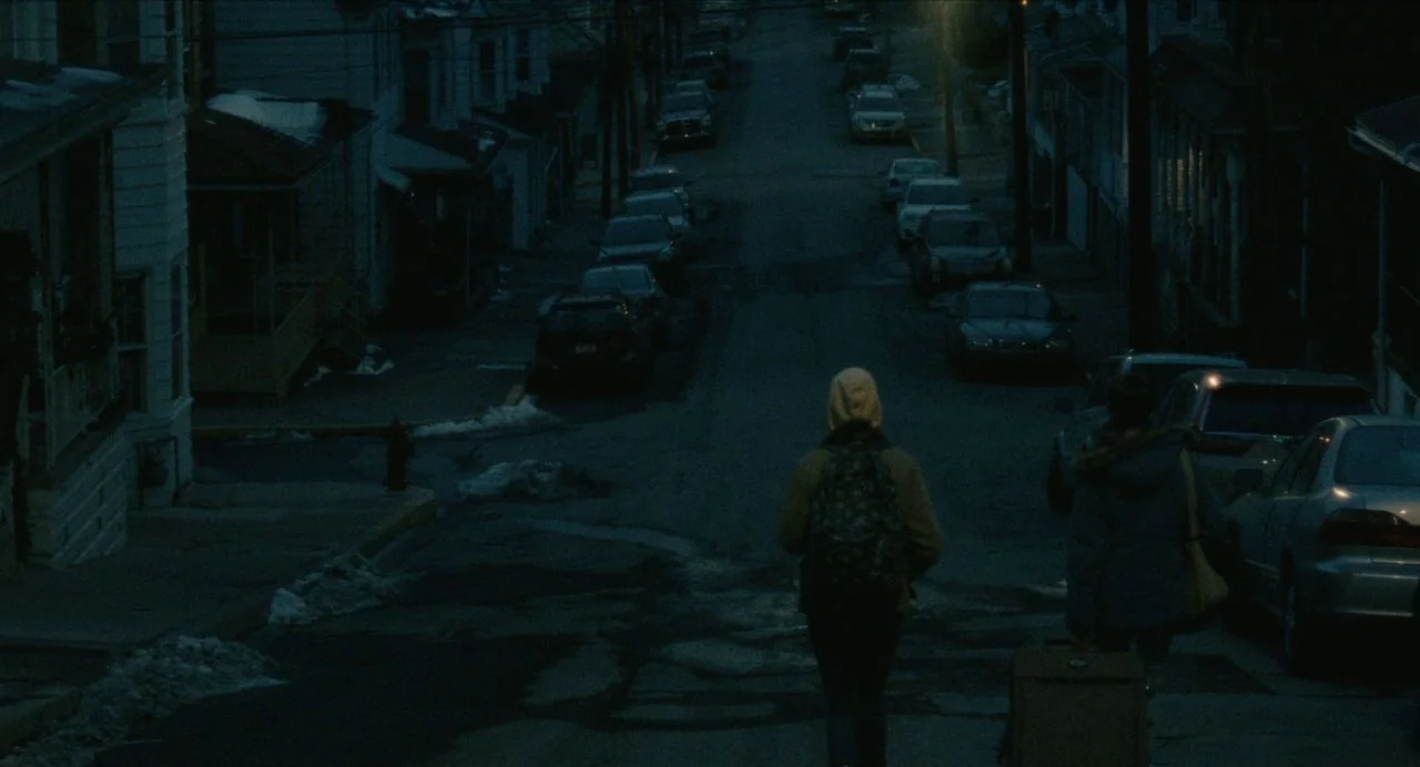Never Rarely Sometimes Always (2020) movie still: wide — A quiet residential neighborhood street at night features rows of cars parked along…