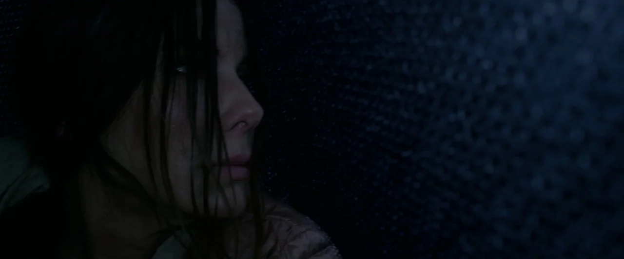 Bird Box (2018) movie still: closeup — A dark, cramped interior space features a coarse, dimly lit wall surface. A woman presses her face against…