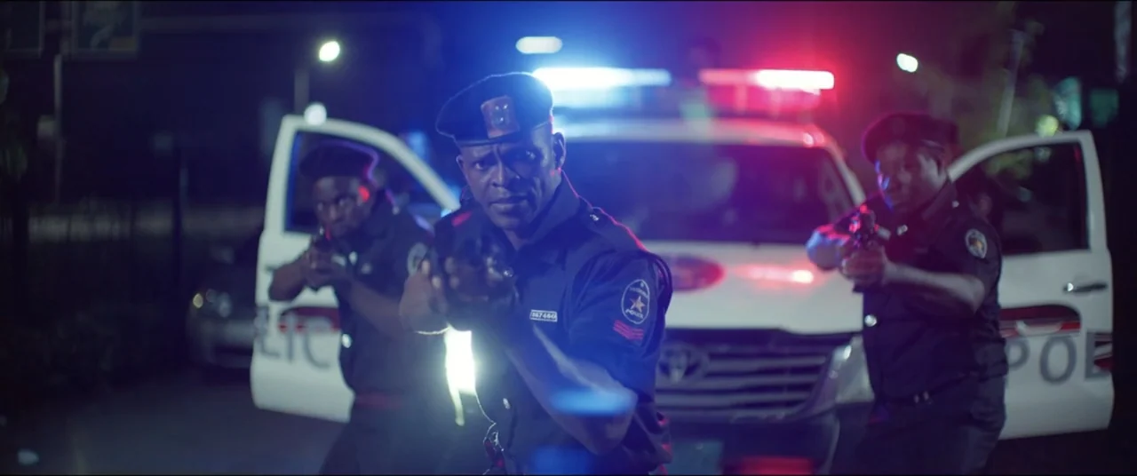 Saving Onome (2024) movie still: medium — Three police officers stand at night before a white patrol vehicle with flashing lights. Each officer…