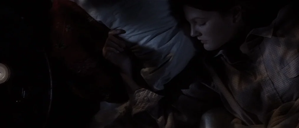 Donnie Darko movie still: closeup — A dark, dimly lit bedroom at night features a person resting on a bed. The individual lies with their head on a…