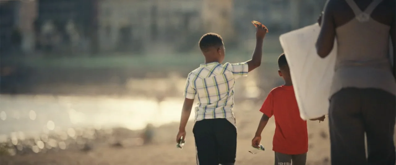 Giannis: The Marvelous Journey (2024) movie still: fullbody — Two children and an adult walk along a sandy coastline during late afternoon. The trio…