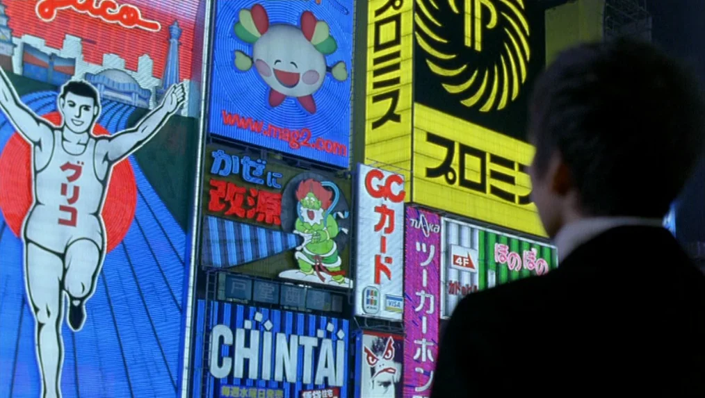 Last Life in the Universe (2003) movie still: medium — A dense urban environment features large, brightly lit digital billboards in a night scene. A…