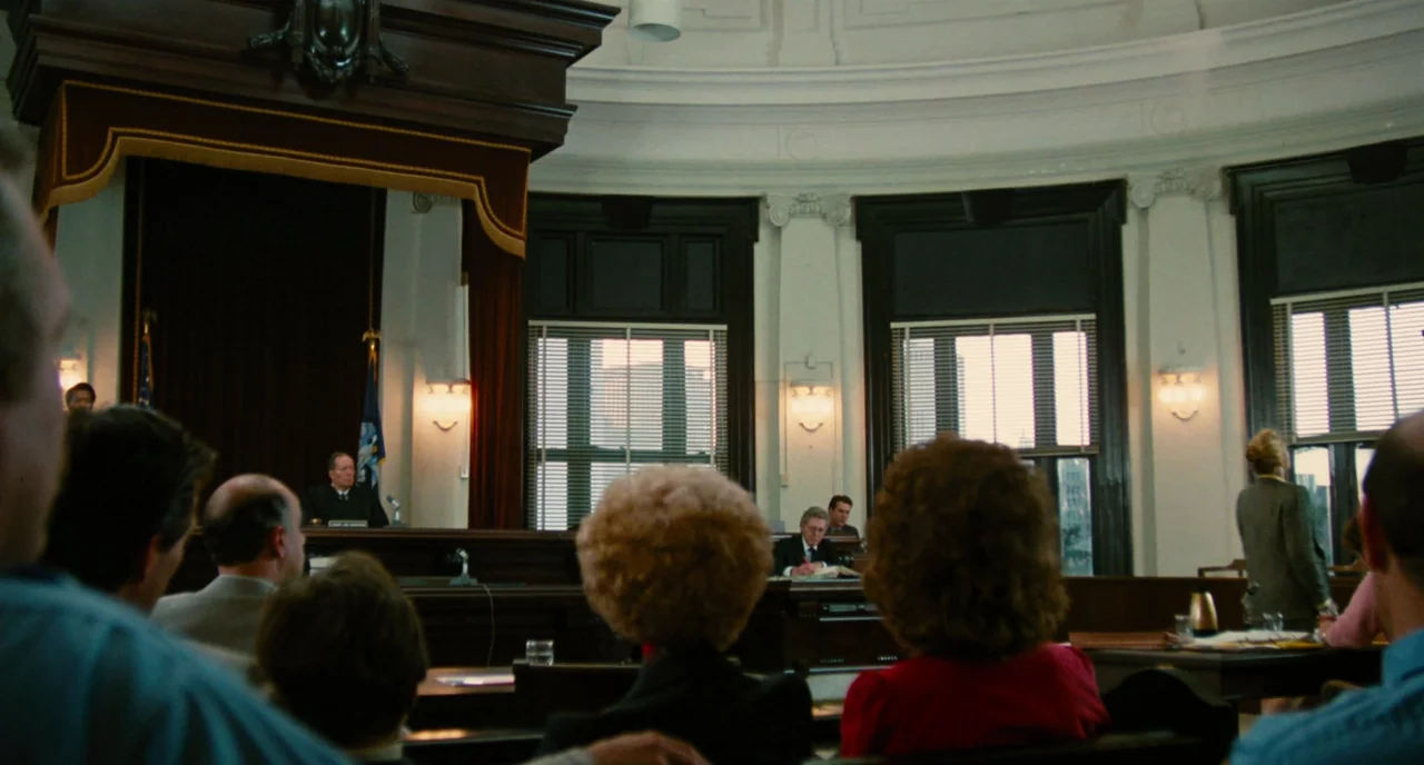 The Big Easy (1986) movie still: wide — A spacious courtroom features high ceilings, dark wood paneling, and large windows with blinds. Numerous…
