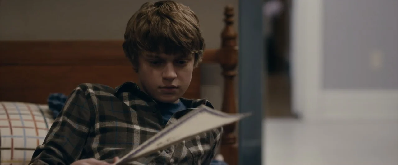 Coming Through the Rye (2016) movie still: medium — A room with a wooden bed frame and a blurry background door frame. A young man with light brown…