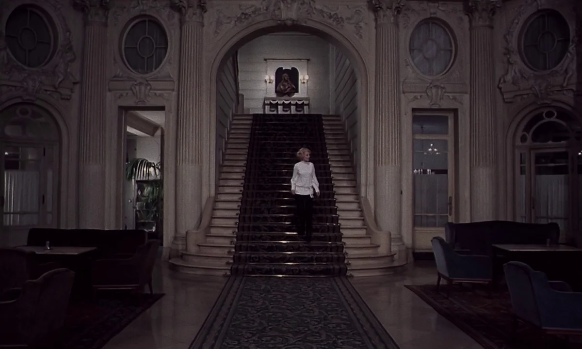 Daughters of Darkness (1971) movie still: wide — A grand hotel lobby features ornate columns and a central staircase with patterned carpet. A single…