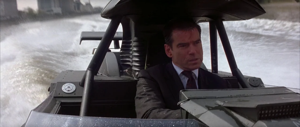 The World is Not Enough (1999) movie still: medium — A man drives a tactical speed boat across a wide river at high velocity. The scene takes place…