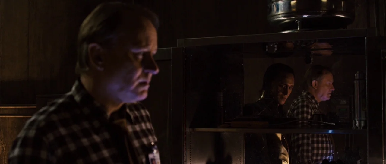Thor (2011) movie still: medium — A dimly lit research lab features dark metal shelving and equipment. An older man stands in the foreground as a…