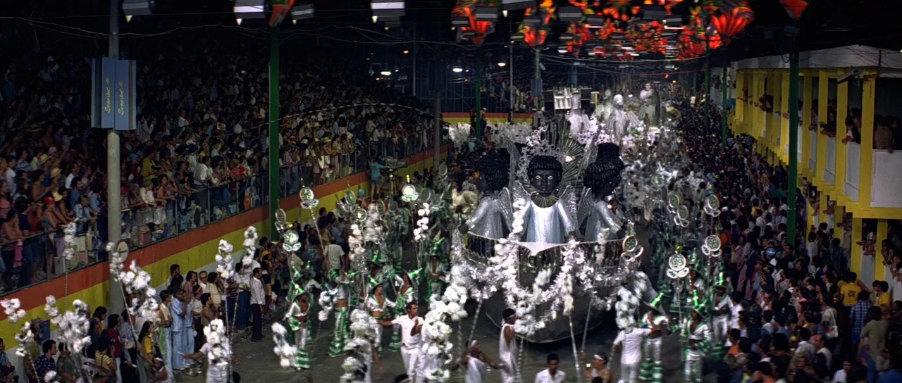 Moonraker (1979) movie still: wide — A nighttime carnival parade moves through a large stadium filled with crowds of spectators. Performers in…