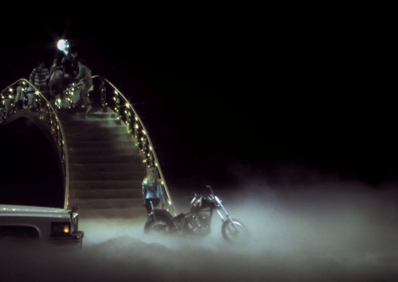 Human Highway (1982) movie still: wide — A decorative arched pedestrian bridge at night sits partially obscured by a thick ground fog. A person…