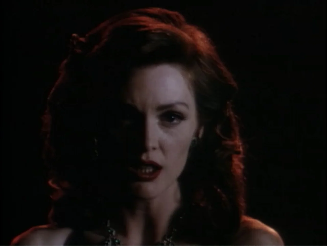 Cast a Deadly Spell (1991) movie still: closeup — A woman stands in a dark interior space with no background detail visible. She faces the camera…