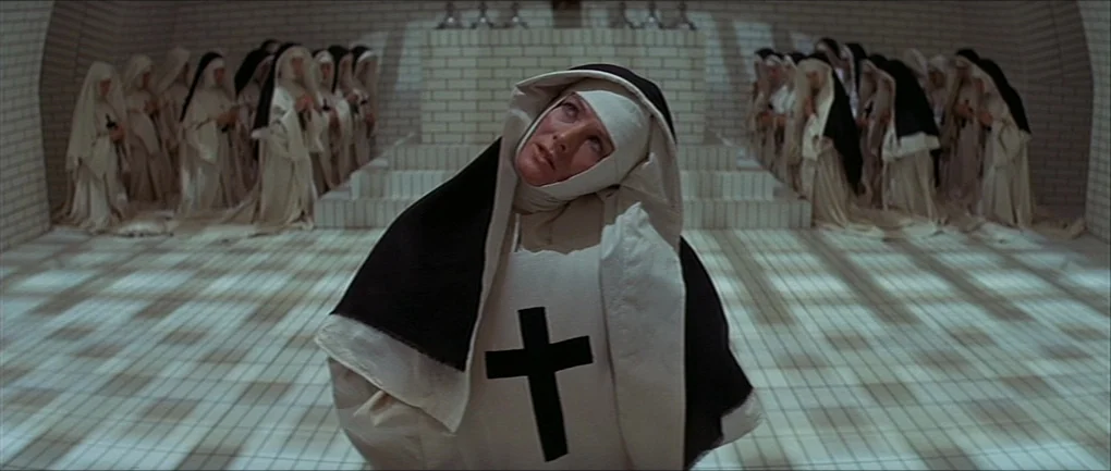 The Devils (1971) movie still: medium — A tiled room with tiered rows of women dressed in full religious habits standing. A primary subject in the…
