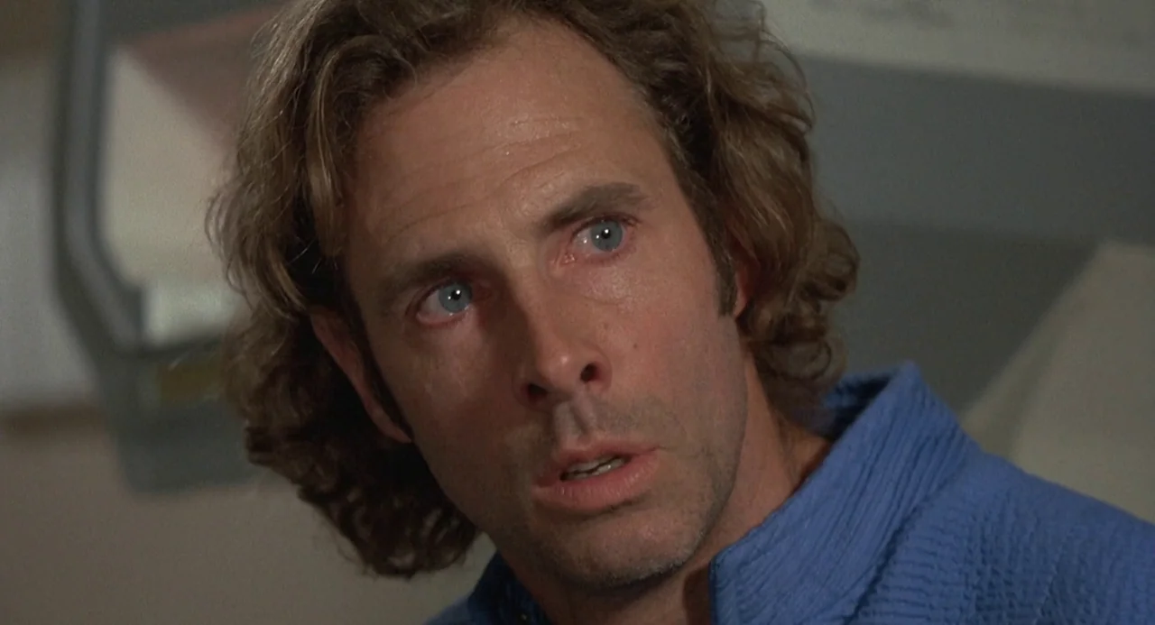 Silent Running (1972) movie still: closeup — A dimly lit, metallic interior with neutral walls forms the backdrop. A man looks off-camera with a…