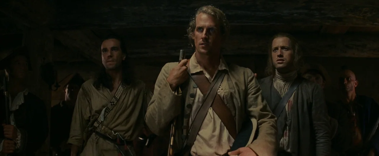 The Last of the Mohicans (1992) movie still: medium — An interior space framed with rough-hewn timber walls and dimly lit ceiling beams. Three men…