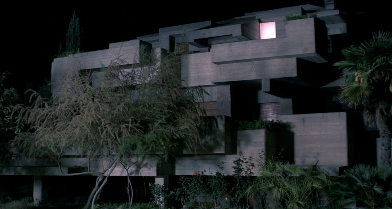 Tenebre (1982) movie still: establishing — A multi-level brutalist concrete house stands amidst dark foliage at night. One solitary window on the…