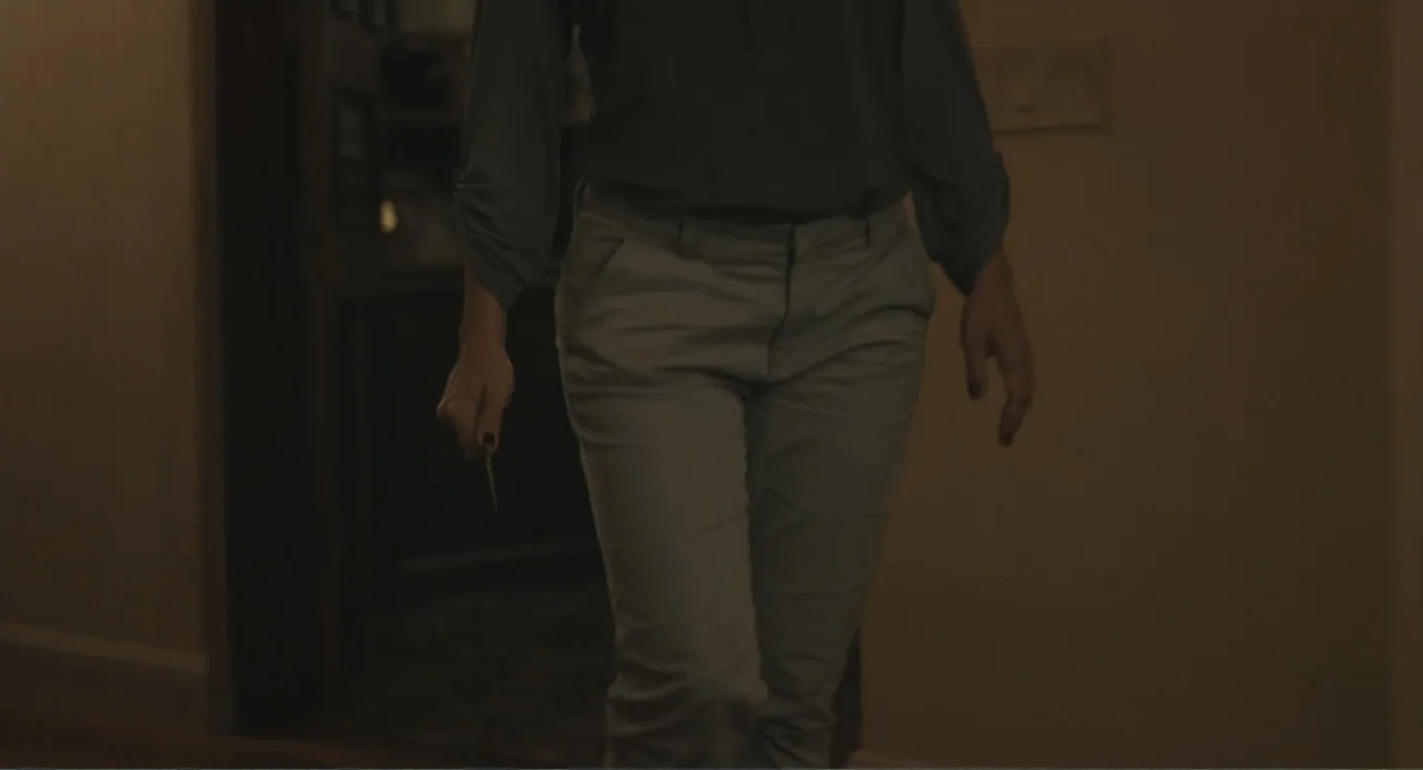 Beatriz at Dinner (2017) movie still: medium — A dimly lit indoor hallway with plain walls and shadows obscuring the background details. A person…