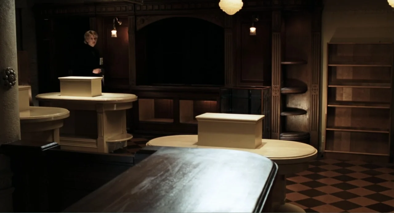 You've Got Mail (1998) movie still: wide — A dark, wood-paneled room contains several oval tables holding white boxes. A woman stands in the…