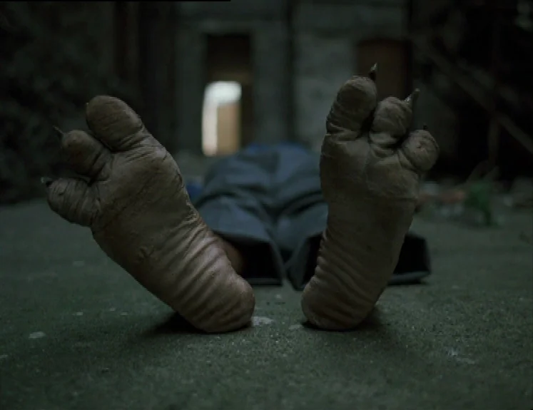 The Brother From Another Planet (1984) movie still: closeup — A dark concrete basement floor has a creature resting in the shadows. Large, textured,…