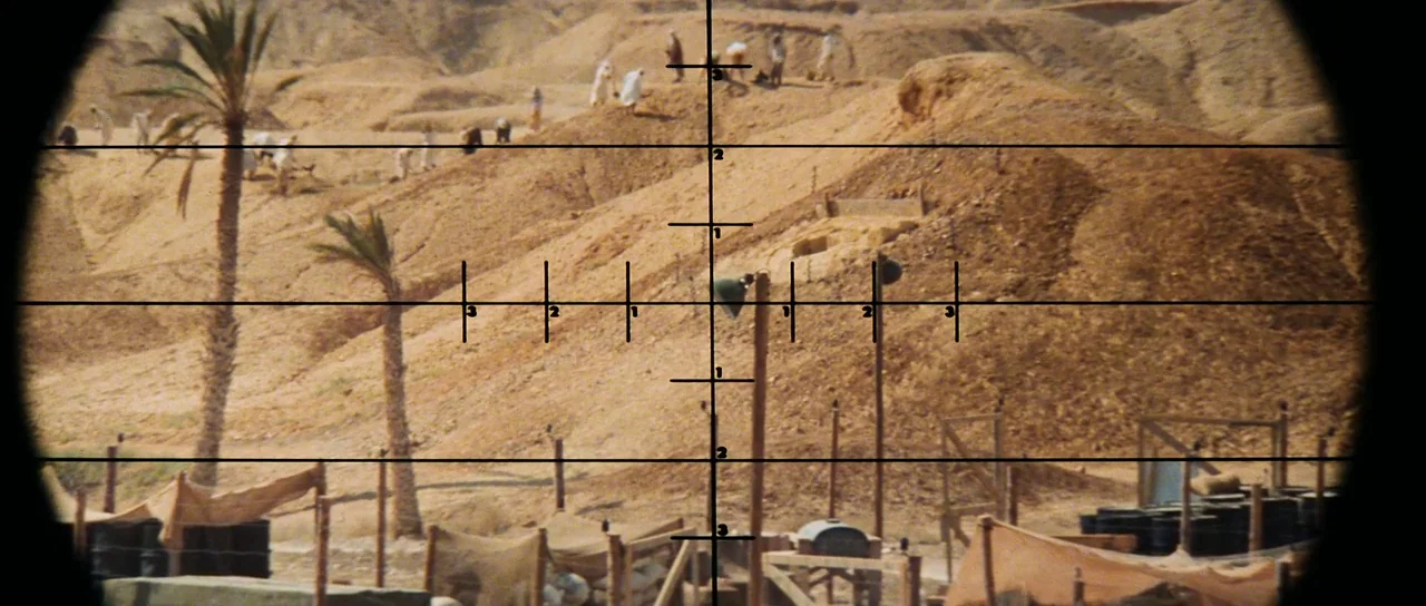 Raiders Of The Lost Ark (1981) movie still: wide — A dry, sandy landscape features a cluster of palm trees and wooden structures. Several small…
