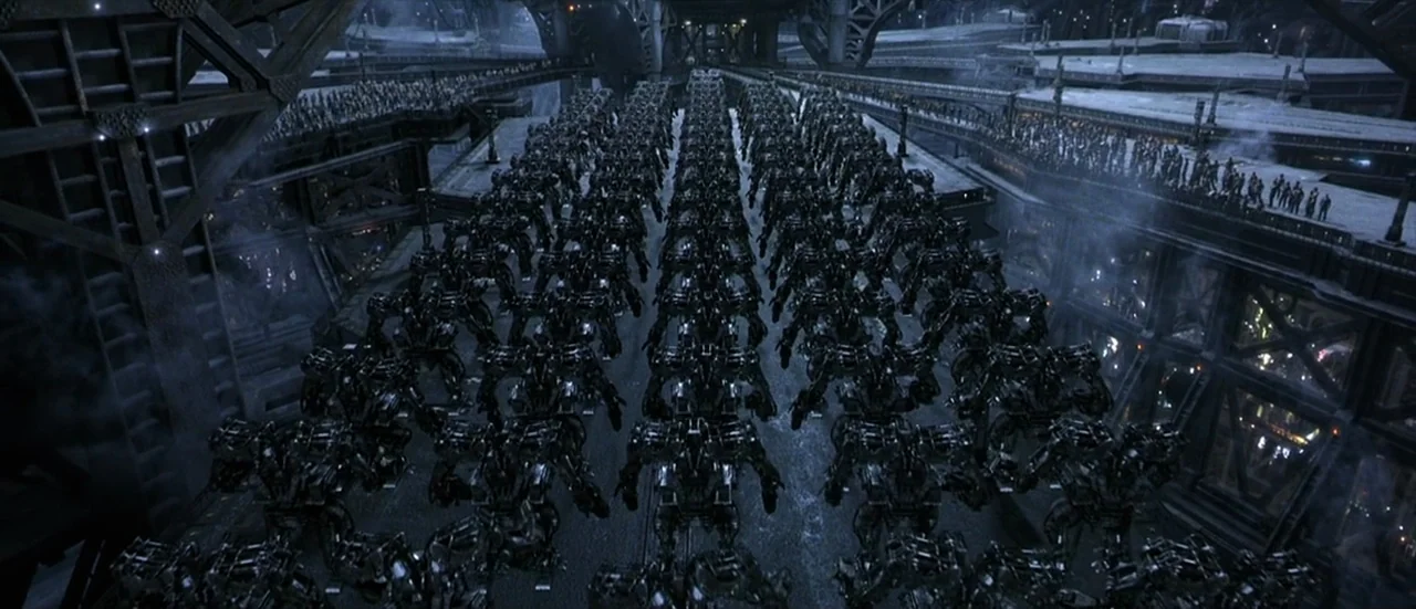 The Matrix Revolutions (2003) movie still: wide — A vast, multi-level industrial superstructure spans the frame in a futuristic setting. Hundreds of…