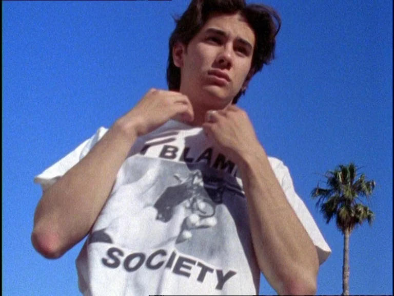 Totally F***ed Up (1993) movie still: medium — A clear, cloudless deep blue sky serves as the backdrop behind a young man. A single tall palm tree…