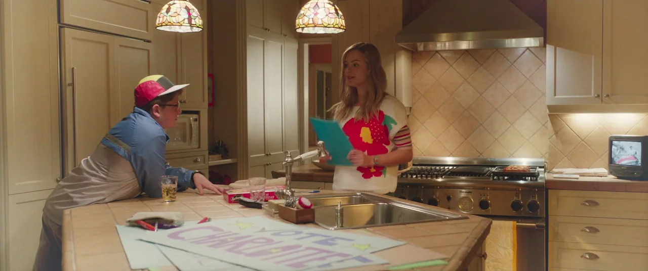 Long Shot (2019) movie still: medium — A spacious domestic space with beige cabinetry and tiled countertops. A young woman and a young man stand on…