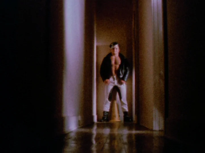 Scorpio Rising (1963) movie still: fullbody — A narrow domestic hallway with dark walls fades into shadow at the lower end. A man wearing a black…