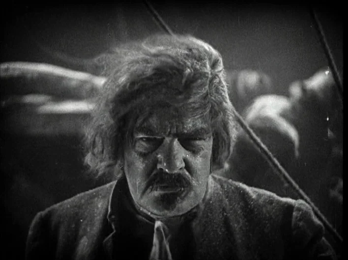 The Man Who Laughs (1928) movie still: closeup — The deck of a ship at night with rigging visible in the background. A man with disheveled hair and…