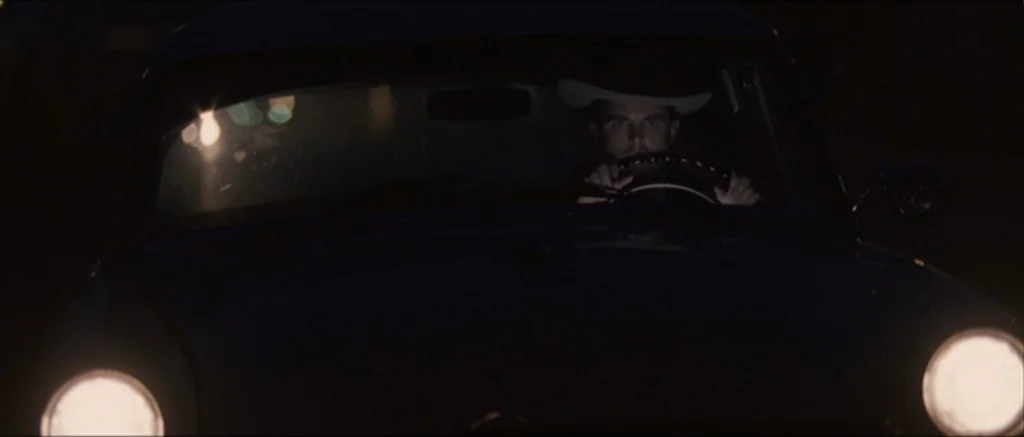 The Killer Inside Me (2010) movie still: medium — A man drives a car through the darkness at night. The headlights illuminate the road ahead from…