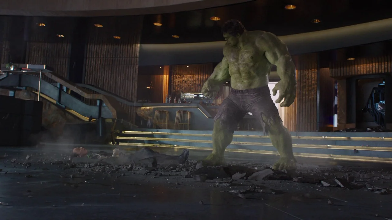The Avengers (2012) movie still: wide — A luxury interior with dark wood wall paneling and a large, cracked floor. The Hulk looms over a man lying…