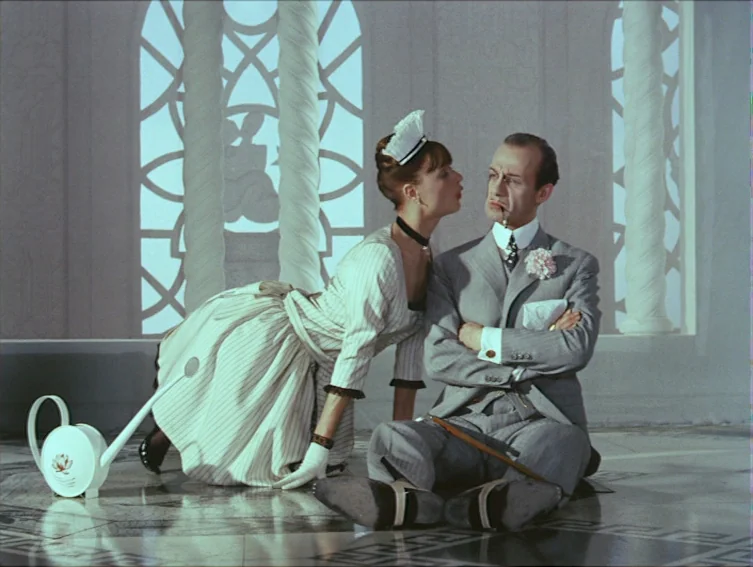 All These Women (1964) movie still: medium — A high-ceiling conservatory features white spiral columns and large glass windows with geometric…