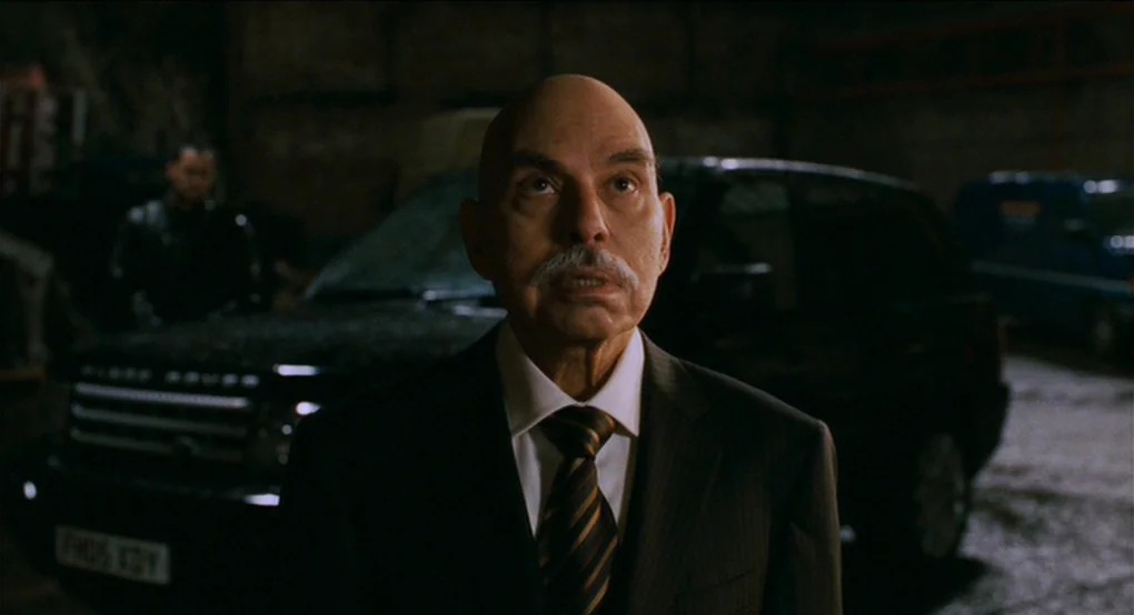Eastern Promises (2007) movie still: medium — A dark parking garage at night contains a black SUV parked behind a man. The older man in a suit looks…