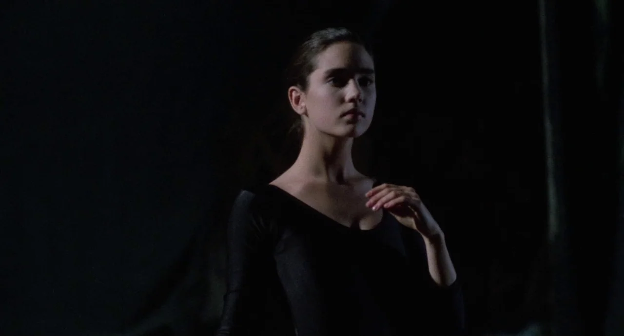 Etoile (1989) movie still: medium — A performer stands in a dark environment with no visible background details. The woman wears a black leotard and…