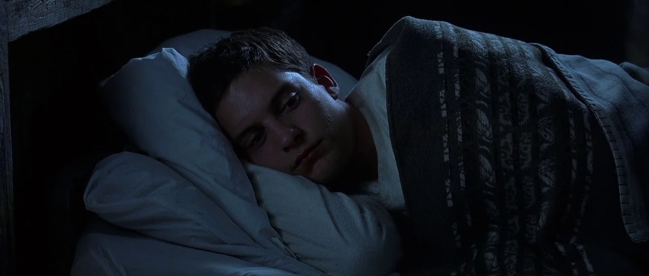 The Cider House Rules movie still: closeup — A dark bedroom at night features a young man lying in bed under covers. The subject rests his head on a…